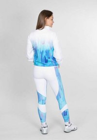 Atletische outfit met een witte jas met een blauw gradient patroon en bijpassende legging met gedurfde, blauwe abstracte vormen.