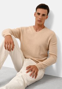 Beige v-hals trui van zachte stof, gecombineerd met off-white broek. De mouwen zijn aansluitend, met geribbelde manchetten en een gladde textuur.