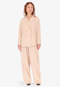 Blazer beige doppiopetto con due tasche, bottoni grandi e pantaloni abbinati a gamba larga in un tessuto morbido e liscio.