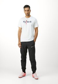 Hvid t-shirt med "PARIS" trykt i marineblå og rød. Sorte joggere med hvidt Nike-logo. Lyserøde fodboldstøvler med snørebånd og gummisåler.