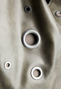 Harmaa materiaali, jossa on sileä pinta, sisältää kolme metallista läpivientiä eri kokoisina, kaksi hopeista ja yksi tummemmassa sävyssä.