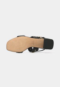 Black heeled sandal with a smooth leather upper, thin straps, a square toe, and a slightly textured beige sole. Features gold hardware accents.