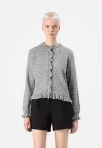 Grå strikket cardigan med rund hals, bølget knaplukning og volangkant. Lange ermer med volangmanchetter.