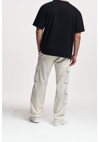 Svart bomulls-T-shirt ihop med cremefärgade cargobyxor med flera sidofickor och vita sneakers, sedd bakifrån.