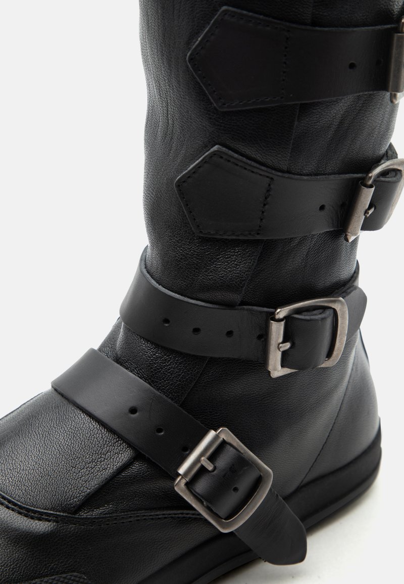 Stivale nero in pelle fino al polpaccio con tre cinturini regolabili e fibbie di metallo argentato su materiale testurizzato.