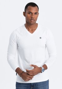 Langärmliges weißes V-Ausschnitt-Shirt aus weichem Baumwollmaterial, mit einem kleinen Logo auf der Brust und einer schlanken Passform.