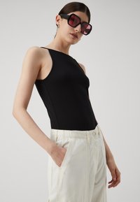 Body senza maniche nero con un design aderente, abbinato a pantaloni larghi di colore chiaro con tasche laterali. Grandi occhiali da sole neri.