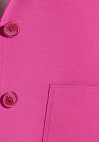 Fuchsia top met een gladde textuur, voorzien van een grote roze knoop en een functionele patch pocket met zichtbare stikdetails.