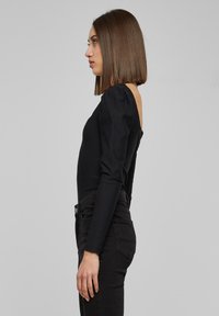 Sort, rillede bodysuit med lange pufærmer og åben ryg, kombineret med sorte højtaljede jeans. Glat tekstur, tætsiddende design.