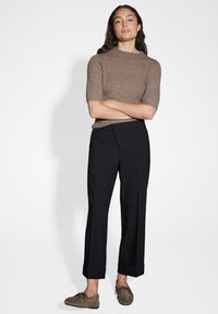 Brown ribbed short-sleeve top paired with black tailored pants featuring folded cuffs. Model wears brown suede slip-on shoes.