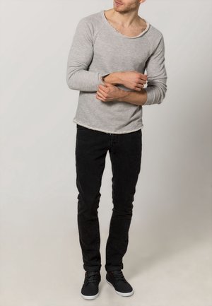 Chemise grise à manches longues avec ourlet brut, associée à un jean noir slim et des baskets noires. Design simple, texture douce, coupe confortable.