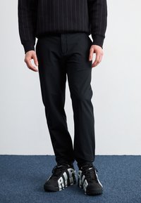 Sorte, slim-fit bukser med en glat tekstur, parret med kraftige sorte sneakers med fed hvid skrift og et robust såledesign.