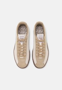 Baskets en suède beige et cuir avec des accents marron, bout rond, lacets plats et semelles intérieures à motifs. Logo Puma affiché sur la languette.