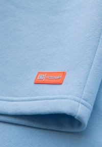 Sweatshirt bleu clair avec une texture douce, ornée d'une étiquette rectangulaire orange affichant "LEVEL UP" et des détails de couture visibles.
