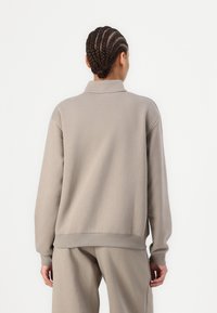 Helehall pullover kõrge kaelusega, langevate õlgadega ja soonikute äärtega. Esitatud pehme, siledas kangas ja mugavas lõikes.