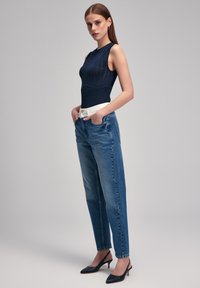 Bodysuit sin mangas de color navy con diseño texturizado, combinado con jeans de tiro alto de color azul claro. La modelo lleva zapatos de tacón negros.