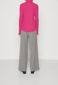 Tajt passande långärmad topp i varmrosa med ståkrage, matchad med vida grå byxor och svarta kraftiga klackar. Textur i ullblandning.