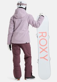 Snowboard outfit featuring a lavender waterproof jacket, maroon pants, white snowboard with pink "ROXY" logo, and black boots.