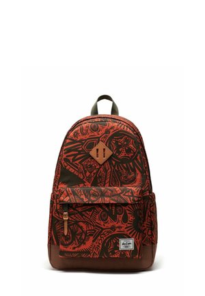 Sac à dos rouge et noir à motifs avec un fond marron, comprenant un patch en forme de losange, une poche avant zippée et des bretelles réglables.