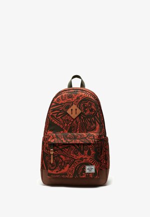 Sac à dos rouge et noir à motifs avec un fond marron, comprenant un patch en forme de losange, une poche avant zippée et des bretelles réglables.
