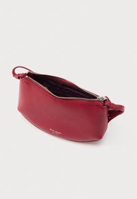 Rdeča torbica iz usnja s ukrivljeno obliko, z zadrgo in zapestnim trakom. Notranjost podložena s temno tkanino, z diskretnim logotipom.
