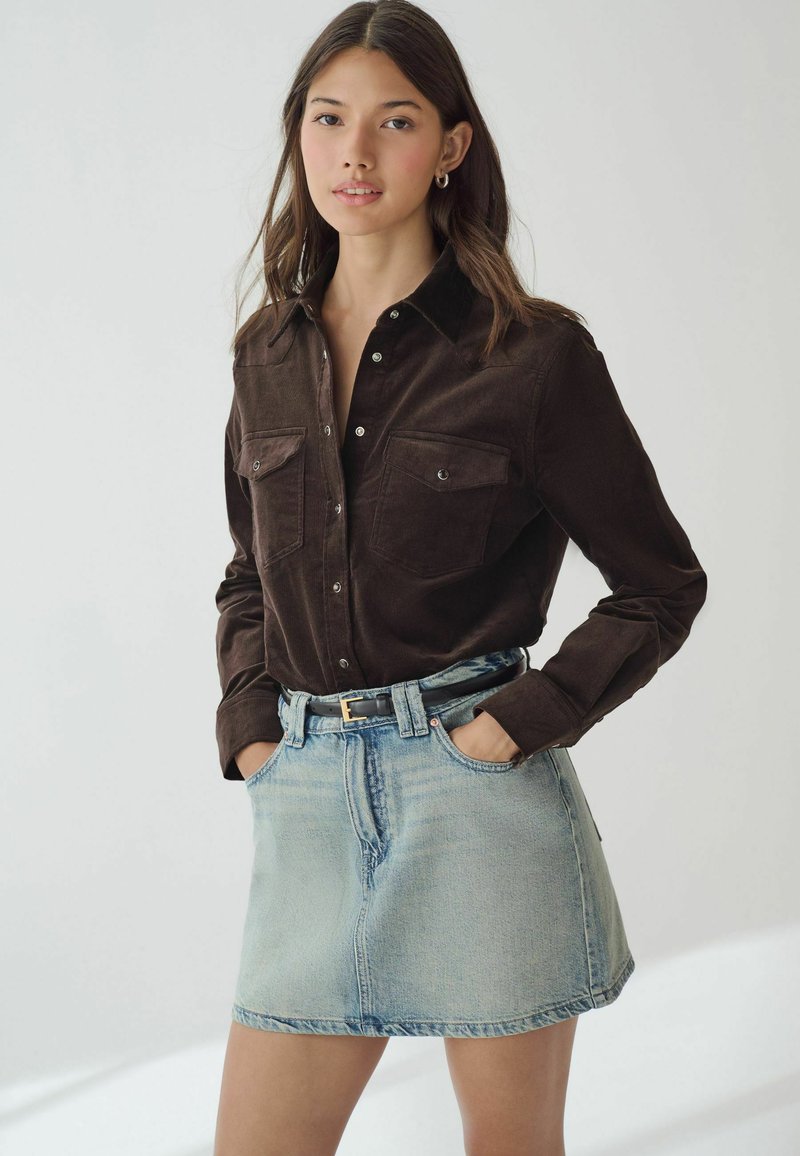 Brun fløjlsskjorte med sort krave, to lommer, knaplukning; parret med lys blå denim A-line nederdel og sort bælte.