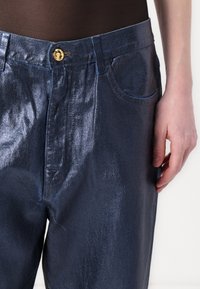 Vaqueros de denim azul marino metálico con una textura suave, que presentan un botón dorado, bolsillos frontales y un diseño de corte relajado.