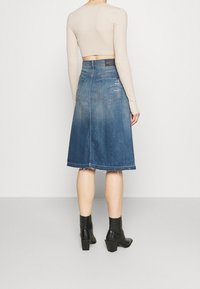 Jeans A-linje kjol med fransad nederkant, ljus till mörkblå gradient, med två bakfickor och medelhög midja. Matchas med svarta klackstövlar.