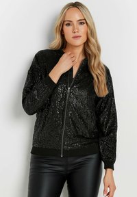 Giacca bomber nera con paillettes, dotata di zip frontale, polsini e orlo a coste. La texture è lucida, riflettendo la luce e creando un motivo sofisticato.