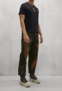 Musta lyhythihainen t-paita valkoisella tekstillä, yhdistetty kuluneisiin mustiin farkkuihin, joissa on ruskeita läiskiä, sekä beigeihin paksupohjaisiin saappaisiin.