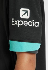 Svart atletisk tröja med en turkos ribbad mudd. Inkluderar en vit "Expedia"-logotyp och en uppåtriktad pilsymbol på ärmen.