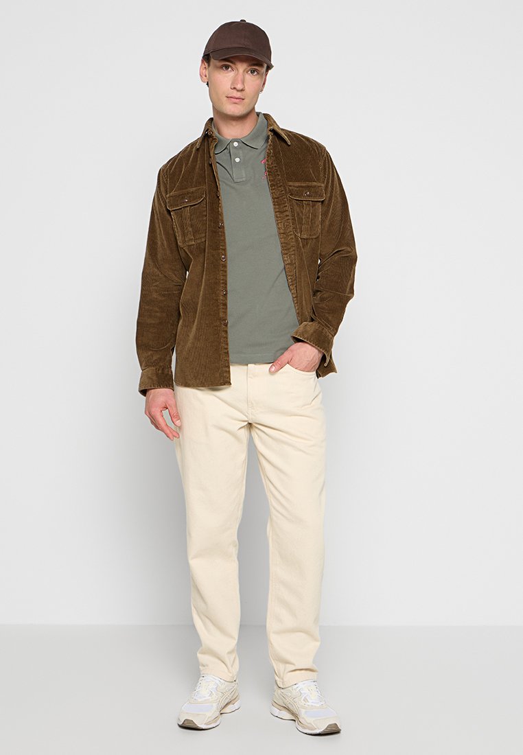 Brown corduroy shirt jacket over a gray polo, beige pants, and gray sneakers. The cap is brown. Features include buttons and pockets.