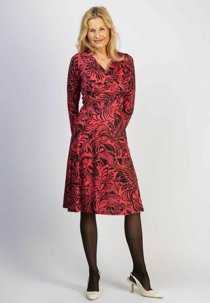 Rot und schwarz gestreiftes Langarmkleid mit floralem Muster, V-Ausschnitt, figurbetontem Bund und ausgestelltem Rock. Kombiniert mit schwarzen Strumpfhosen und cremefarbenen Absätzen.