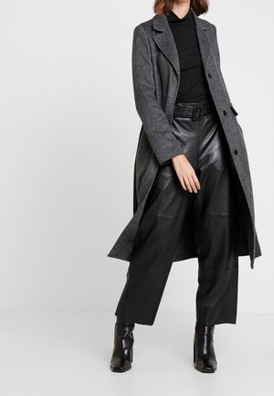 Manteau en chevrons gris avec revers sur un col roulé noir, associé à un pantalon en cuir noir à jambes larges et des bottines.