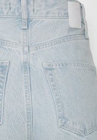 Světle modré džínové kalhoty s vysokým pasem, dvěma zadními kapsami a strukturovanou tkaninou. Součástí je malý, vyražený logotyp na pásku pasu.