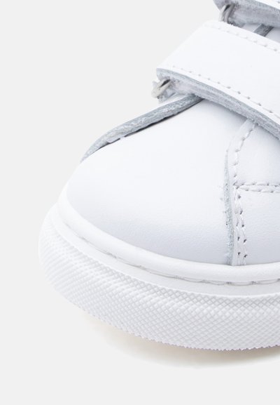 Λευκό δερμάτινο παπούτσι με στρογγυλεμένη μύτη, διαθέτει γκρι λεπτομέρειες και λευκή ελαστική σόλα με υφή. Λουράκι με βέλκρο για εύκολο κούμπωμα.