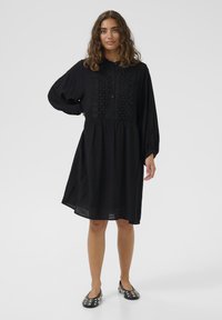 Rochie neagră cu front butonat, având detalii brodate și mâneci lungi. Are o talie strânsă și ajunge deasupra genunchiului.