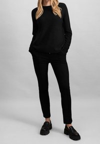 Maglione nero lavorato a maglia abbinato a pantaloni neri aderenti. Entrambi i capi presentano una texture liscia, un design minimalista e sono arricchiti da cuciture sottili.