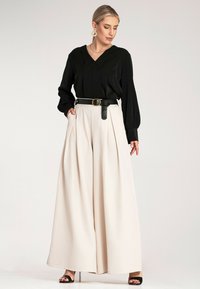 Czarna bluzka z długim rękawem i dekoltem w serek zestawiona z kremowymi spodniami z wysokim stanem i plisami oraz czarnym paskiem z okrągłą klamrą; elegancki i nowoczesny design.