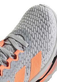 Graue und orangefarbene Laufschuhe mit strukturiertem Strick-Obermaterial, grauen Schnürsenkeln und orangenen Kunststoff-Ösen, Nahaufnahme von Zehenbereich und Seite.