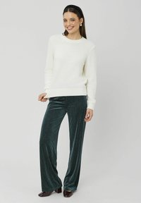 Pull blanc en maille à manches longues associé à un pantalon large en velours côtelé vert. La tenue présente un tissu texturé et une coupe décontractée.