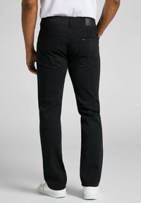 Pantalones vaqueros de mezclilla negra con un corte recto, que presentan una parche de cuero en la cinturilla y dos bolsillos traseros con detalles de costura curvada.
