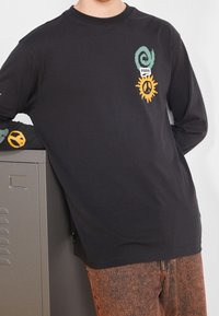 Black long-sleeve shirt made from cotton blend, featuring a green spiral and yellow sun with peace symbol graphics on the chest and sleeve.