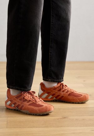 Zapatillas deportivas naranjas con materiales de malla y ante, con acentos en blanco y gris, suela texturizada y diseño con cordones.