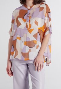 Haut transparent multicolore présentant des formes abstraites en orange, marron et lavande. Fermeture par boutons au niveau de l'encolure, coupe décontractée et manches courtes.