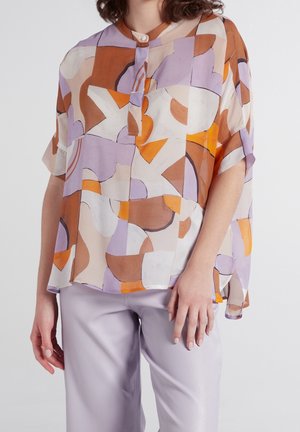 Top trasparente multicolore con forme astratte in arancione, marrone e lavanda. Chiusura con bottoni al collo, vestibilità morbida e maniche corte.
