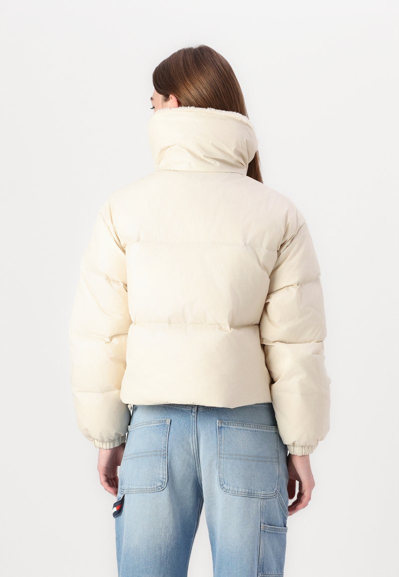 Puffige, kurze Jacke in sanftem Beige mit hohem Kragen und elastischen Manschetten. Das Material erscheint glatt mit einem leichten Glanz.