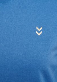 Blå stickad tyg med fin ribbing. Har en liten vit broderad chevronlogga. Slät textur med en ren, konsekvent färg.