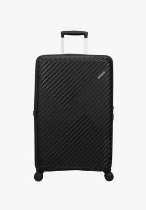 Grande valigia rigida nera con scanalature diagonali, quattro ruote girevoli, manico telescopico e logo "American Tourister" davanti.