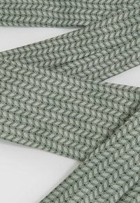 Groene stof met een geometrisch patroon, voorzien van fijne zwarte lijnen en een gladde textuur, gevouwen en gestapeld.